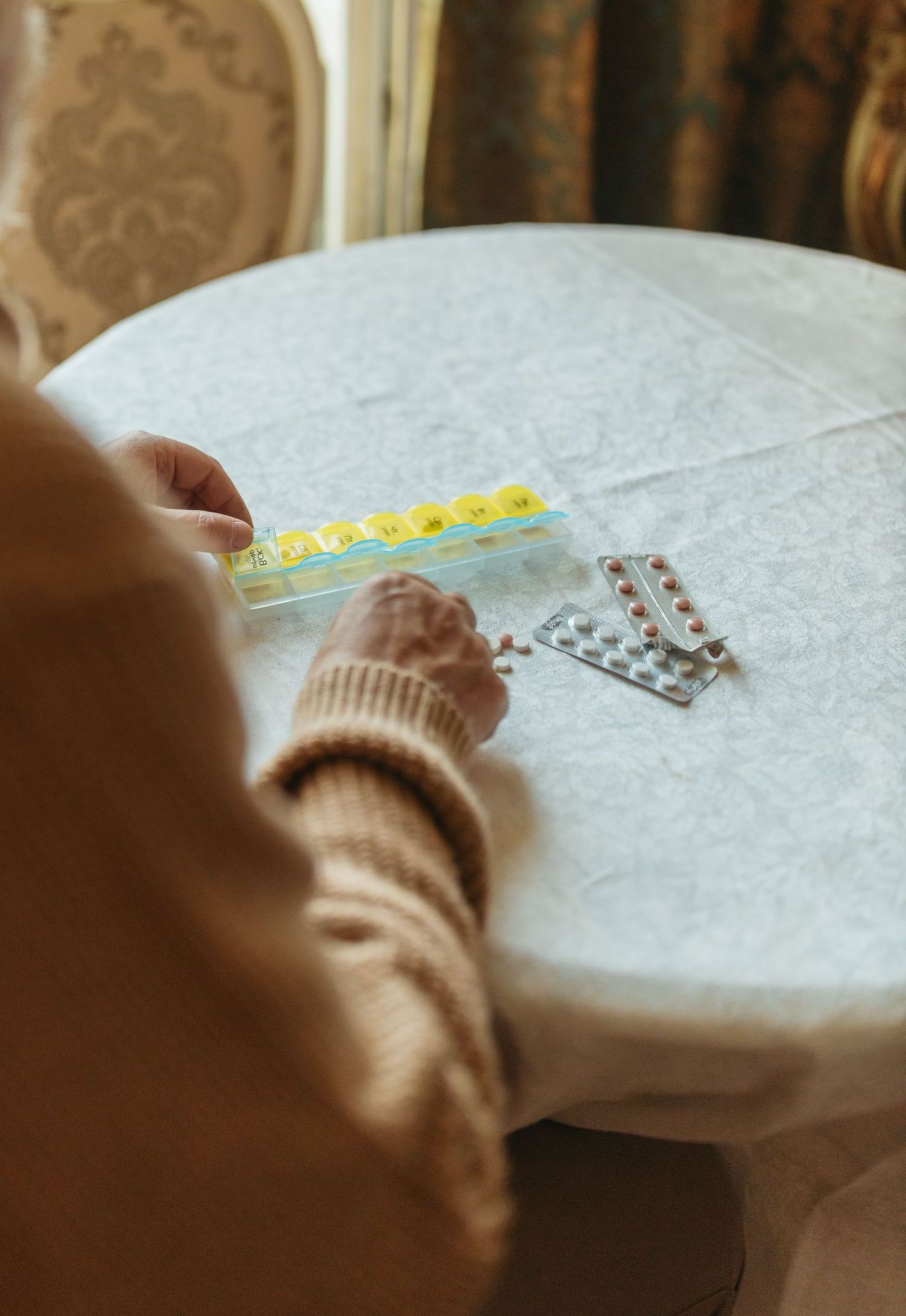 Elderly man sorting pills at a table, focusing on health and wellness.